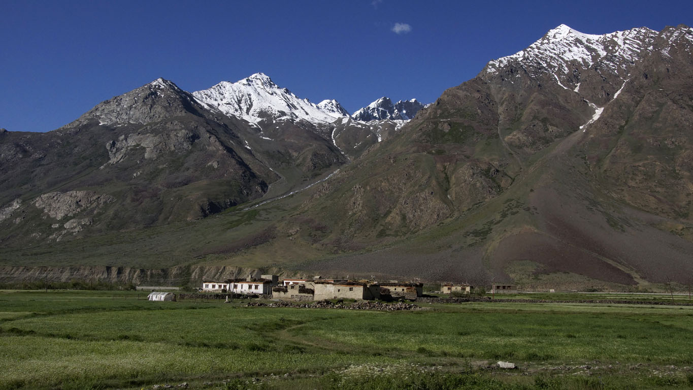minuscule village au pied des montagnes enneigées sur fond de vertes cultures