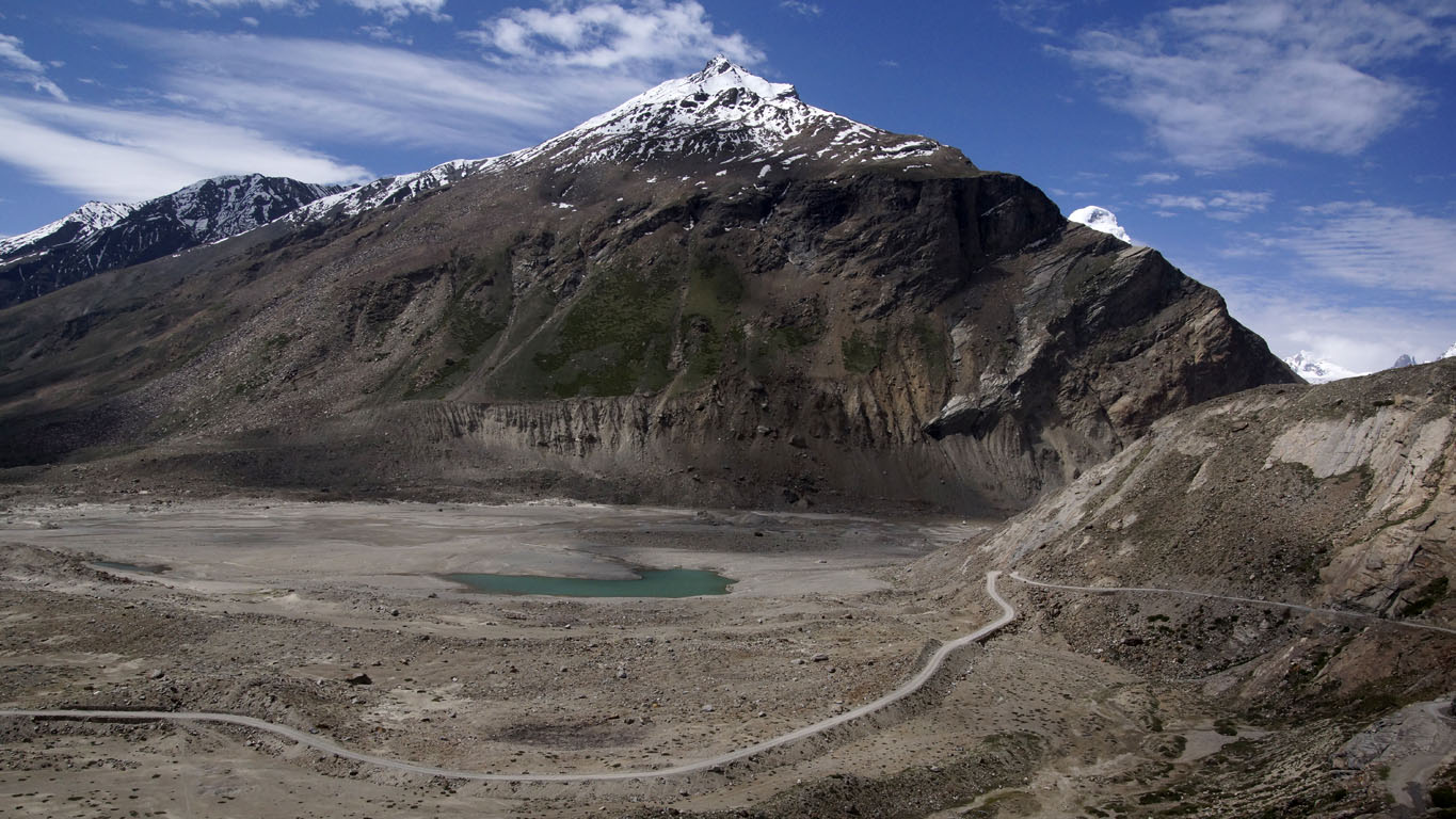 Un serpentin de route longeant un lac turquoise et dominé mar un sommet enneigé Zanskar