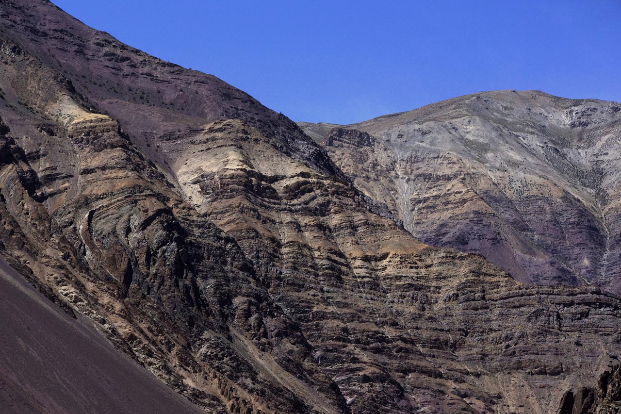 Ici, les couches rocheuses allant du noir au violet en passant par le marron, ocre, beige, ondulent horizontalement en direction de Chilling Ladakh